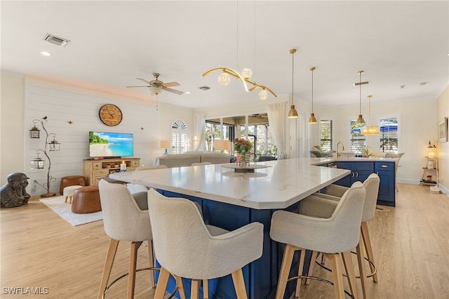 kitchen with blue cabinetry, light countertops, hanging light fixtures, open floor plan, and light wood-type flooring