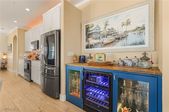 bar with arched walkways, a dry bar, stainless steel appliances, light wood-style floors, and beverage cooler