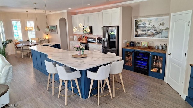 kitchen featuring arched walkways, decorative light fixtures, stainless steel appliances, white cabinetry, and a sink