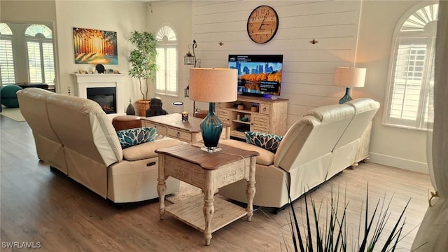 living room featuring a glass covered fireplace, wooden walls, baseboards, and wood finished floors