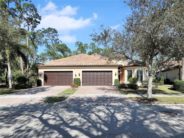 mediterranean / spanish-style home with an attached garage, a tiled roof, decorative driveway, and stucco siding