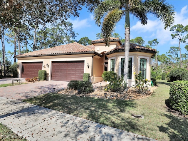 mediterranean / spanish house featuring decorative driveway, stucco siding, an attached garage, a front yard, and a tiled roof