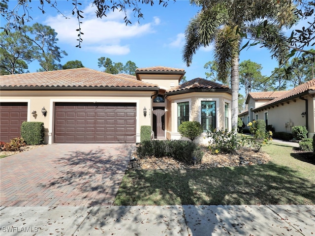 mediterranean / spanish home with an attached garage, a tiled roof, decorative driveway, stucco siding, and a front lawn