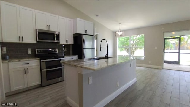 kitchen with white cabinetry, light stone counters, decorative light fixtures, appliances with stainless steel finishes, and a kitchen island with sink