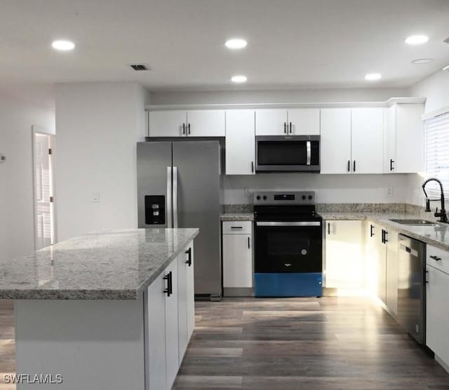 kitchen with sink, stainless steel appliances, light stone countertops, white cabinets, and a kitchen island