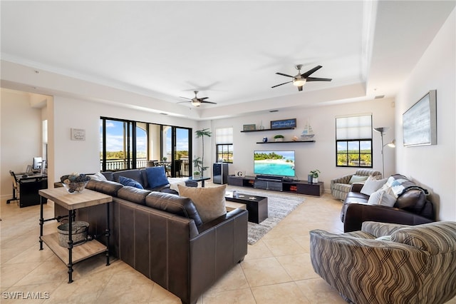 tiled living room with ornamental molding, a healthy amount of sunlight, ceiling fan, and a tray ceiling