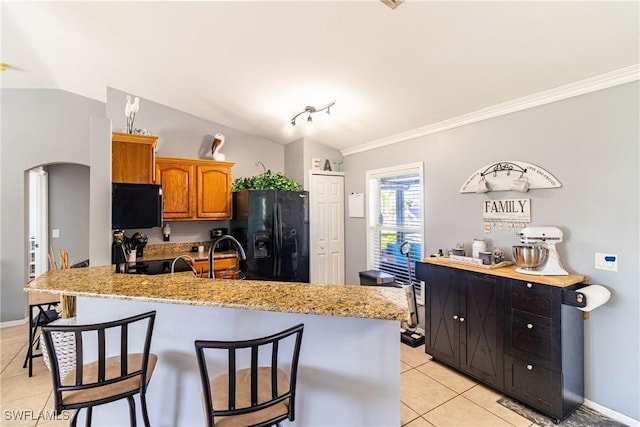 kitchen with black refrigerator with ice dispenser, a breakfast bar, and vaulted ceiling