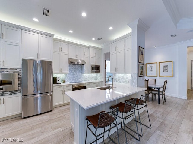 kitchen featuring a kitchen bar, sink, ornamental molding, stainless steel appliances, and light hardwood / wood-style floors