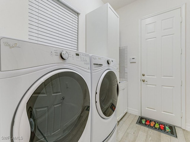 clothes washing area with cabinets, washing machine and dryer, and light hardwood / wood-style flooring