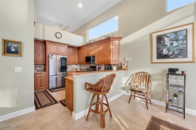 kitchen with a breakfast bar, tasteful backsplash, kitchen peninsula, stainless steel appliances, and a high ceiling