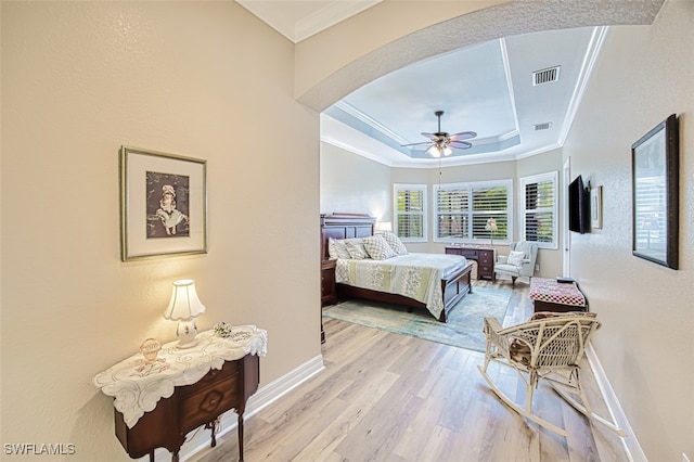 bedroom with crown molding, light hardwood / wood-style flooring, a raised ceiling, and ceiling fan