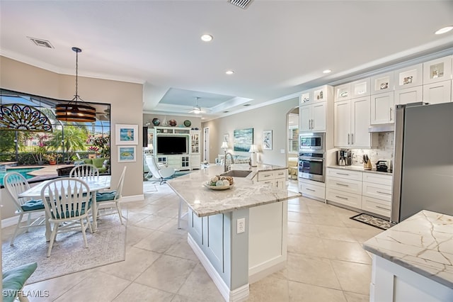 kitchen with sink, white cabinetry, hanging light fixtures, appliances with stainless steel finishes, and a kitchen island with sink