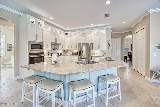 kitchen featuring white cabinetry, stainless steel appliances, light stone counters, and a large island with sink