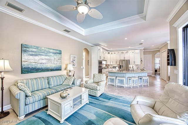 living room with sink, ornamental molding, light tile patterned floors, ceiling fan, and a raised ceiling