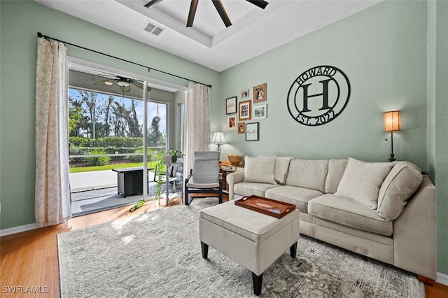 living room featuring hardwood / wood-style flooring, a raised ceiling, and ceiling fan