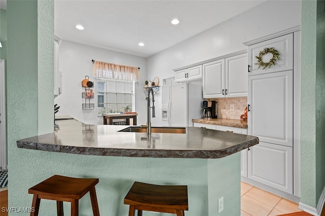 kitchen featuring white cabinetry, white refrigerator with ice dispenser, a breakfast bar area, and kitchen peninsula