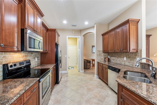 kitchen with tasteful backsplash, sink, dark stone countertops, light tile patterned floors, and stainless steel appliances