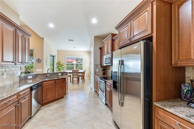 kitchen with sink, stone counters, appliances with stainless steel finishes, tasteful backsplash, and decorative light fixtures