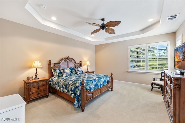 bedroom with light colored carpet, a raised ceiling, and ceiling fan