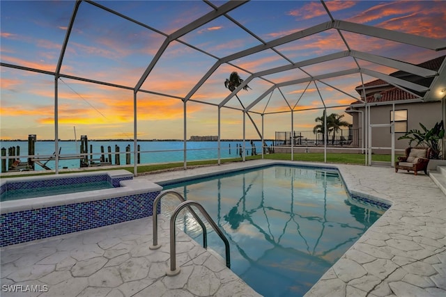 pool at dusk with a water view, a hot tub, a patio area, and glass enclosure