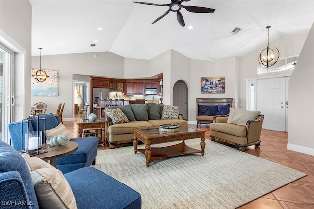 tiled living room with ceiling fan with notable chandelier and high vaulted ceiling