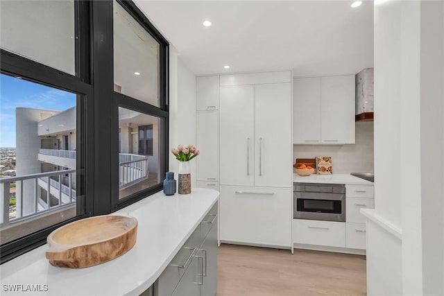 kitchen featuring white cabinetry, wall chimney range hood, light hardwood / wood-style flooring, and stainless steel oven