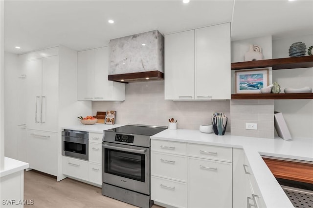 kitchen featuring premium range hood, appliances with stainless steel finishes, white cabinetry, decorative backsplash, and light hardwood / wood-style floors