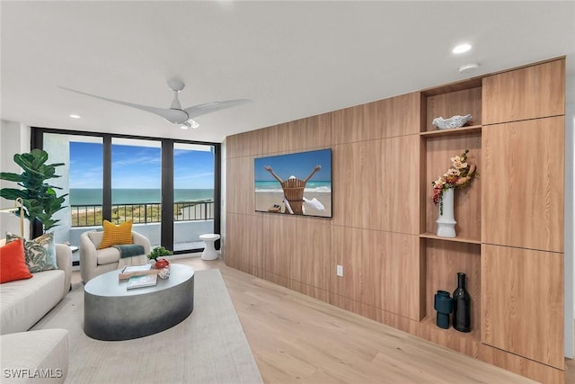 living room featuring a water view, a wall of windows, ceiling fan, and light hardwood / wood-style floors