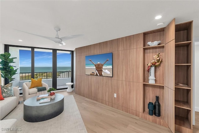 living room featuring ceiling fan, a water view, floor to ceiling windows, and light wood-type flooring