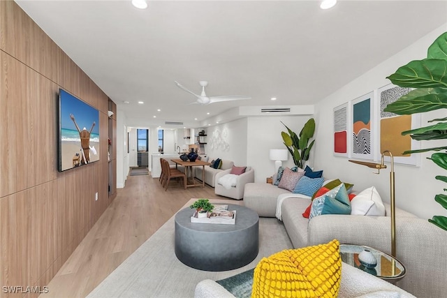 living room with ceiling fan, wooden walls, and light hardwood / wood-style flooring