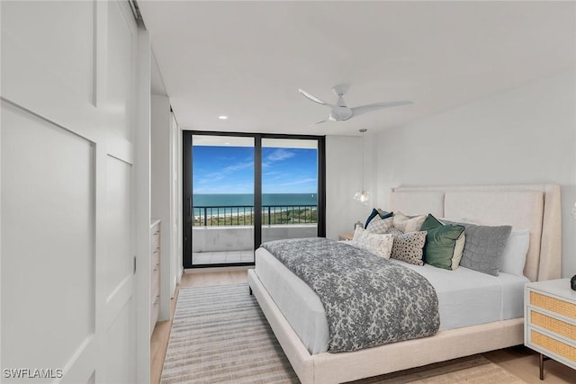 bedroom featuring a wall of windows, ceiling fan, access to exterior, a water view, and light hardwood / wood-style floors