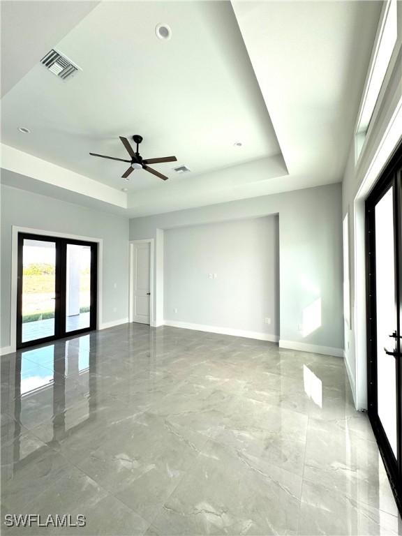 empty room featuring french doors, ceiling fan, and a raised ceiling