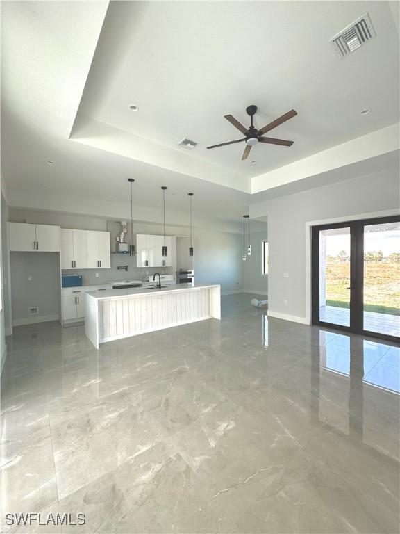 unfurnished living room featuring a raised ceiling and ceiling fan