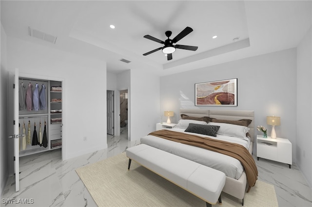 bedroom featuring ensuite bathroom, a walk in closet, ceiling fan, a tray ceiling, and a closet