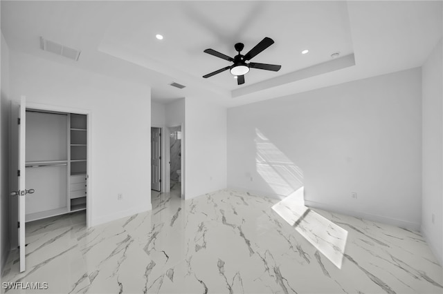 unfurnished bedroom featuring a raised ceiling, ensuite bathroom, a spacious closet, and ceiling fan