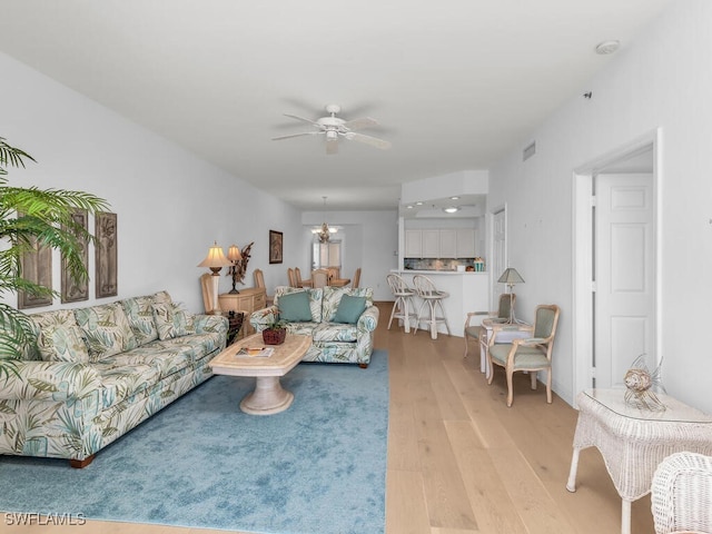 living room featuring ceiling fan with notable chandelier and light hardwood / wood-style floors