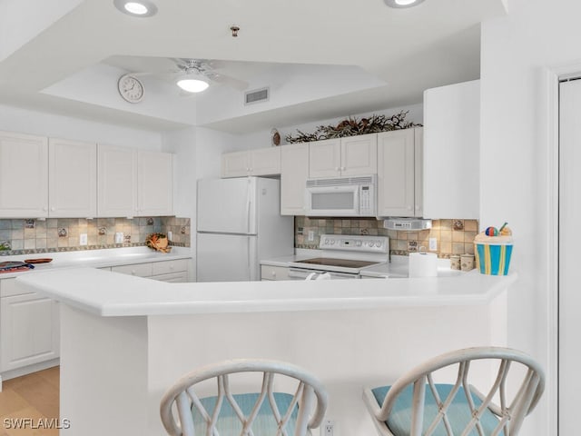 kitchen featuring white appliances, a breakfast bar, ceiling fan, tasteful backsplash, and white cabinets