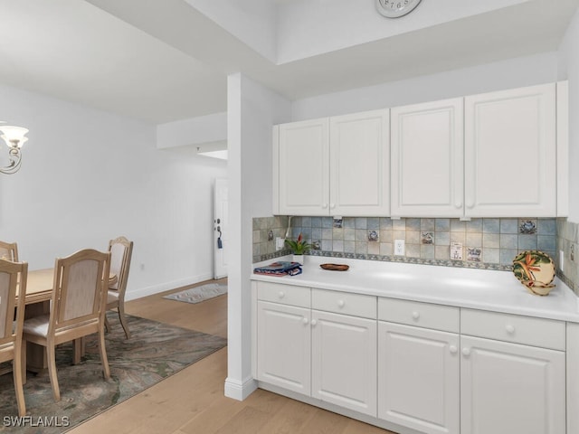 kitchen with decorative backsplash, white cabinets, and light wood-type flooring