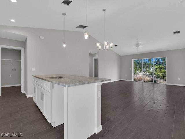 kitchen with lofted ceiling, white cabinetry, hanging light fixtures, a kitchen island with sink, and light stone countertops