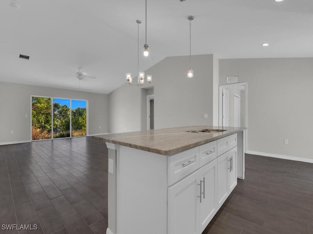 kitchen featuring decorative light fixtures, lofted ceiling, white cabinets, a center island, and light stone counters