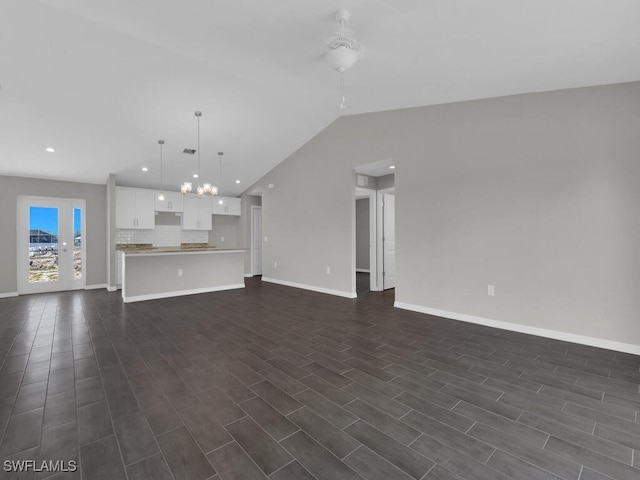 unfurnished living room with vaulted ceiling, ceiling fan with notable chandelier, and dark hardwood / wood-style flooring