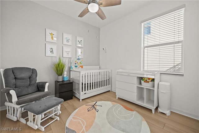 bedroom with a crib, light wood-style floors, baseboards, and ceiling fan