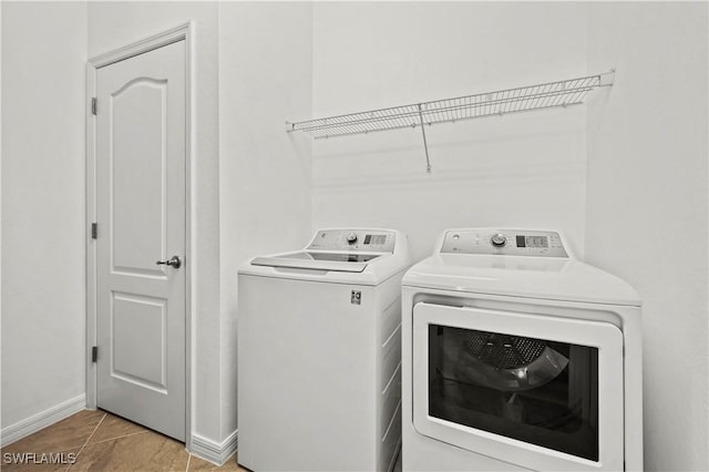 clothes washing area with washer and dryer, laundry area, light tile patterned flooring, and baseboards