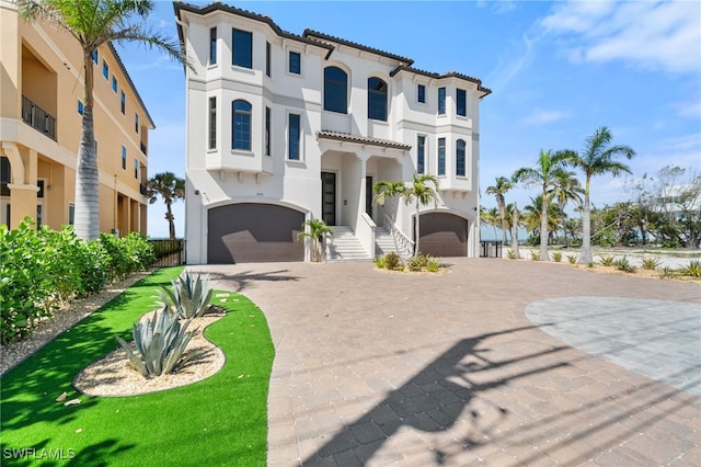 mediterranean / spanish home with a tiled roof, decorative driveway, an attached garage, and stucco siding