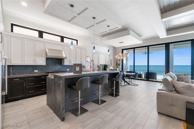 kitchen featuring a water view, a kitchen breakfast bar, backsplash, open floor plan, and extractor fan