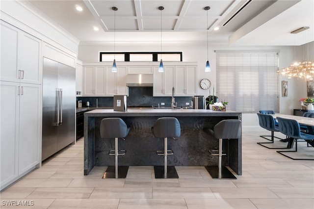 kitchen with pendant lighting, a center island with sink, white cabinets, and built in refrigerator