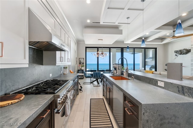 kitchen featuring high end range, a sink, pendant lighting, wall chimney exhaust hood, and tasteful backsplash