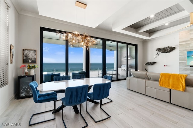 dining room featuring wood finish floors, a water view, a notable chandelier, a tray ceiling, and crown molding