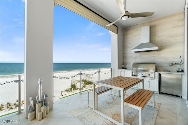 balcony featuring an outdoor kitchen, a grill, a ceiling fan, and a view of the beach