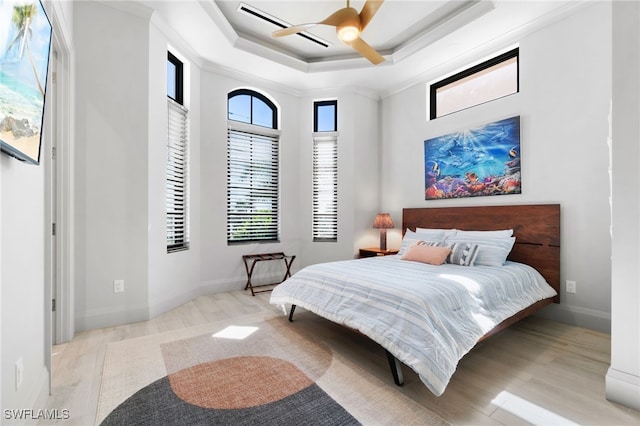 bedroom with ceiling fan, ornamental molding, a tray ceiling, and light hardwood / wood-style floors